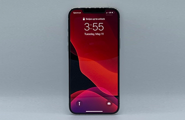 A smartphone is propped up with the screen illuminated showcasing the time.